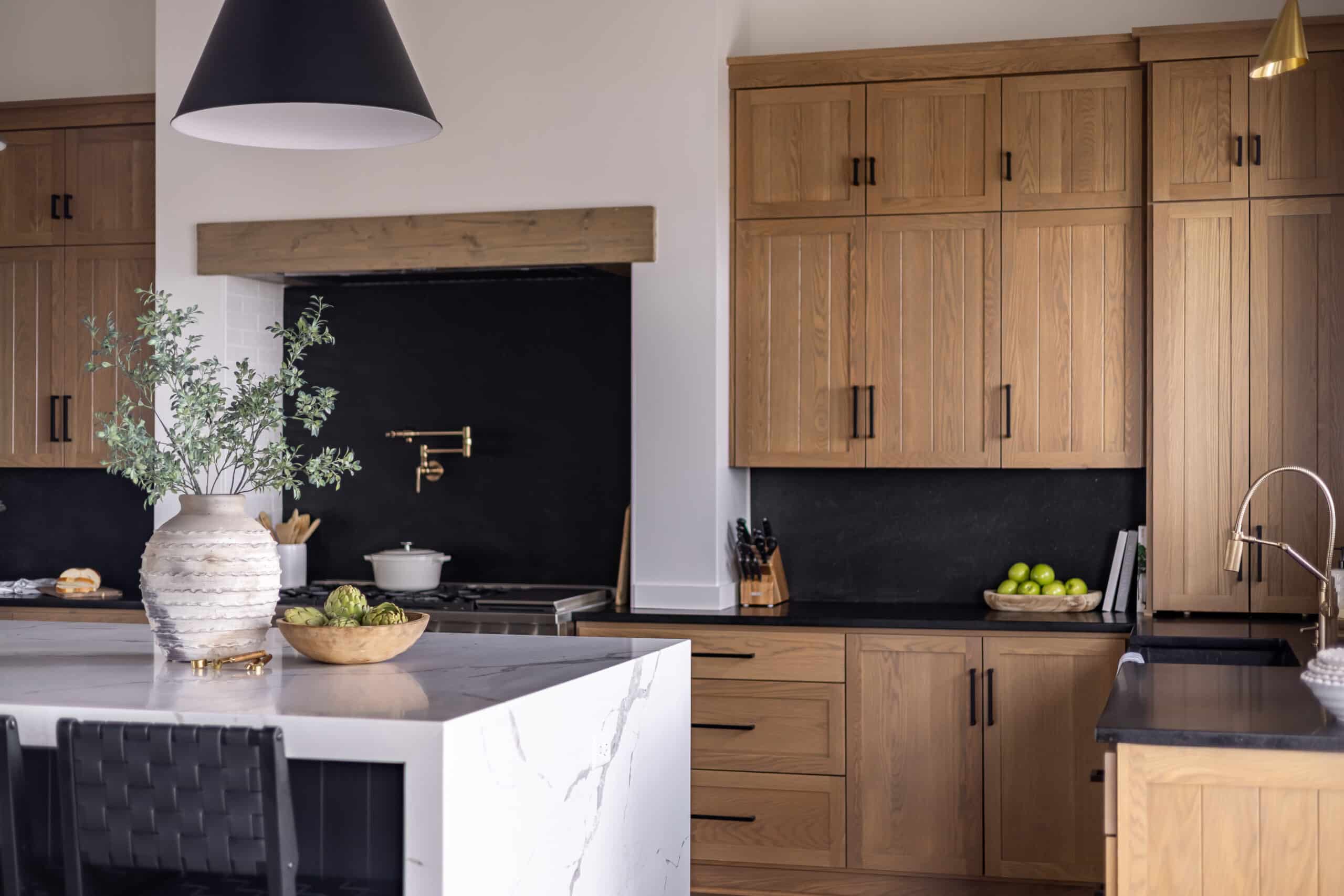 Cuisine moderne avec armoires en bois clair, îlot en marbre blanc veiné, électroménagers noirs, et accents dorés (robinet).