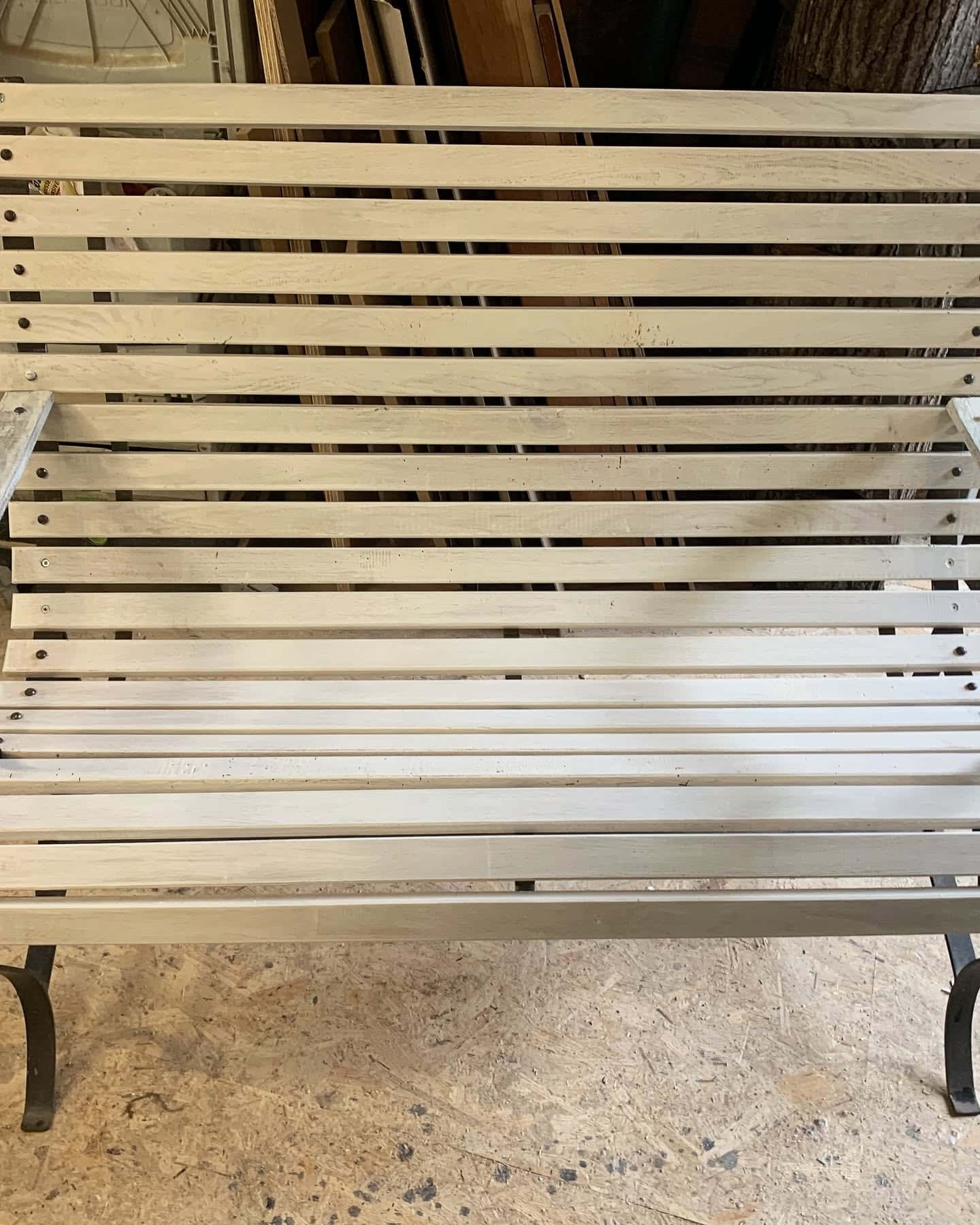 Banc de jardin à lattes en bois clair avec structure en métal noir dans un atelier.