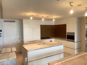 Cuisine moderne blanche avec îlot central en marbre, détails dorés et luminaires en cours d'installation.