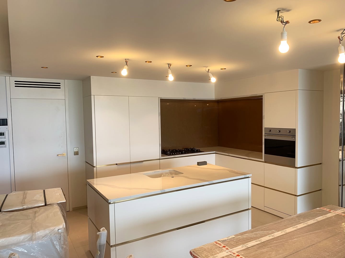 Cuisine moderne blanche avec îlot central en marbre, détails dorés et luminaires en cours d'installation.