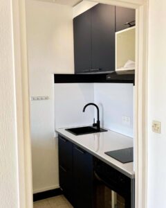 Kitchenette moderne bleu marine et blanc avec évier noir mat et robinet col-de-cygne dans un petit espace.