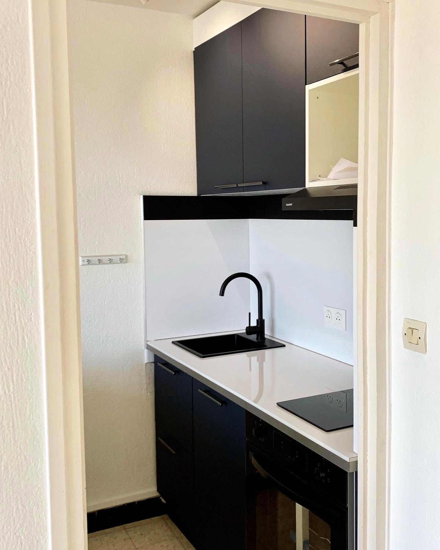 Kitchenette moderne bleu marine et blanc avec évier noir mat et robinet col-de-cygne dans un petit espace.