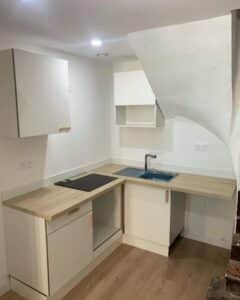 Petite kitchenette moderne sous un escalier avec meubles blancs, plan de travail bois et plaque de cuisson induction.