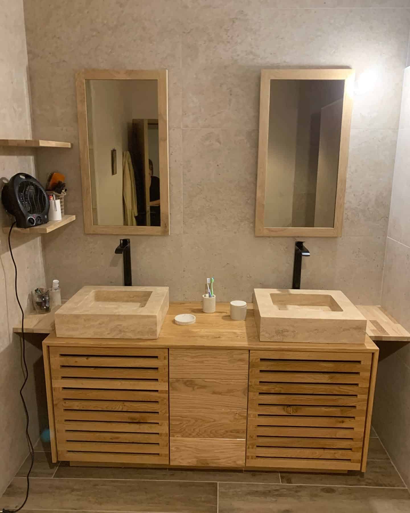 Double vasque en pierre sur meuble bois latté avec robinetterie noire.