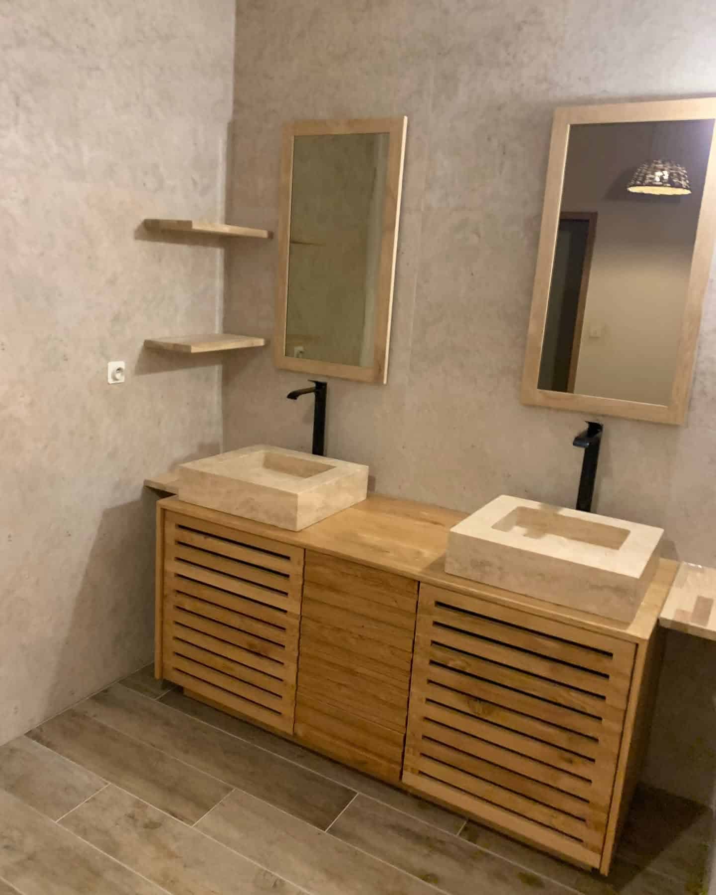 Double vasque en pierre, meuble bois à lattes, robinetterie noire et miroirs assortis dans salle de bain beige.