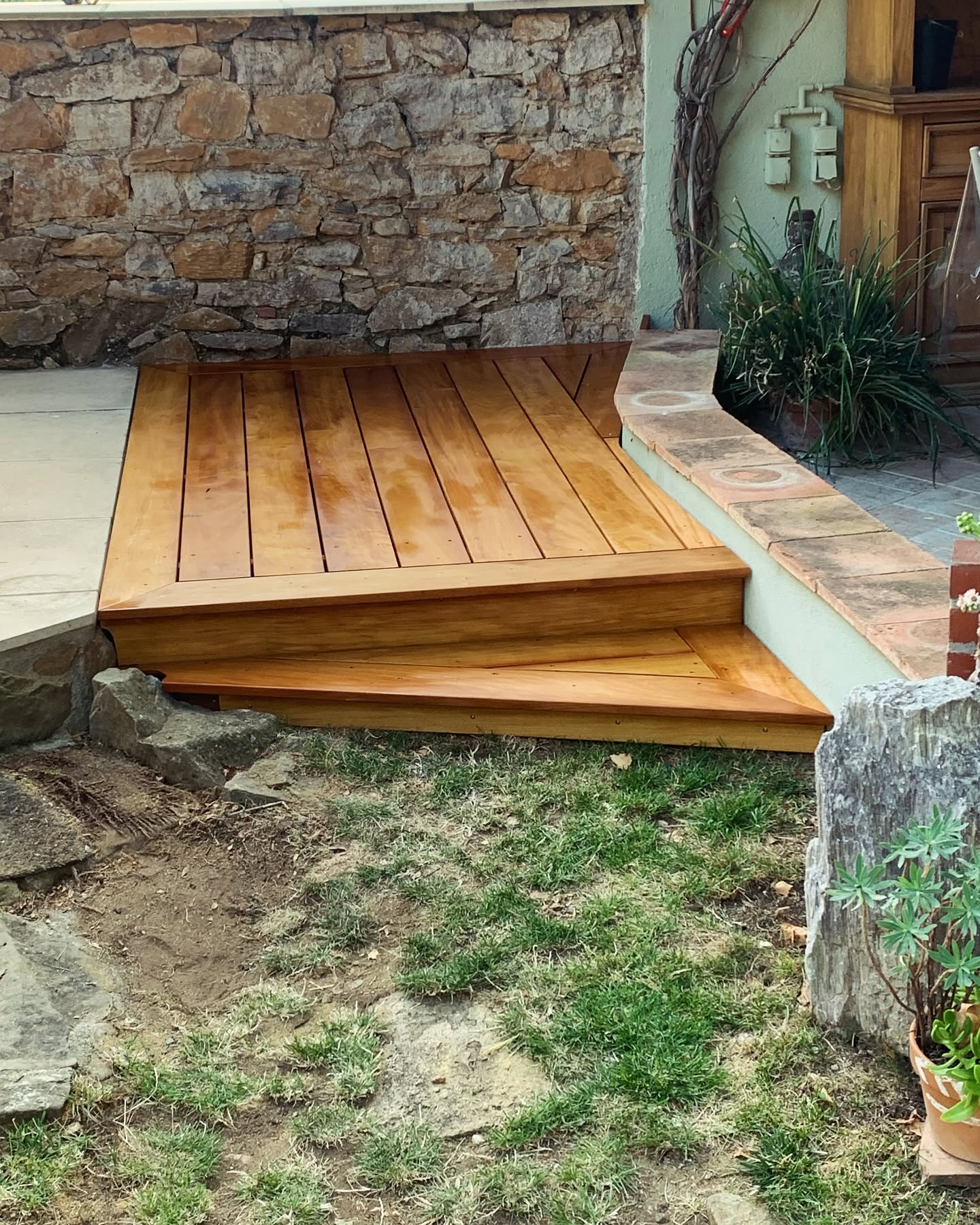 Marches en bois poli pour terrasse de jardin devant un muret en pierre naturelle.
